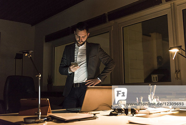 Businessman standing in office at night using smartphone