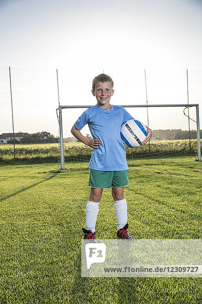 Porträt eines lächelnden jungen Fußballspielers  der den Ball auf dem Fußballplatz hält.