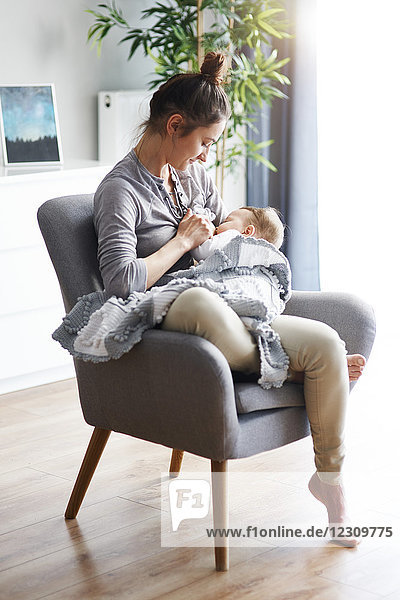 Mother sitting on armchair at home breastfeeding her baby