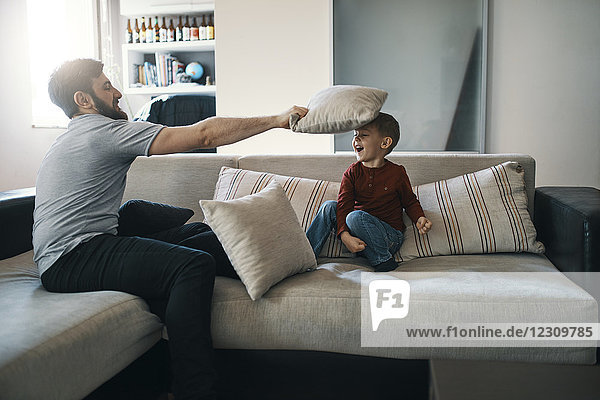 Vater und kleiner Sohn spielen zusammen auf der Couch im Wohnzimmer