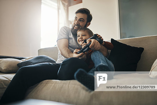 Vater und Sohn sitzen zusammen auf der Couch und spielen ein Computerspiel.