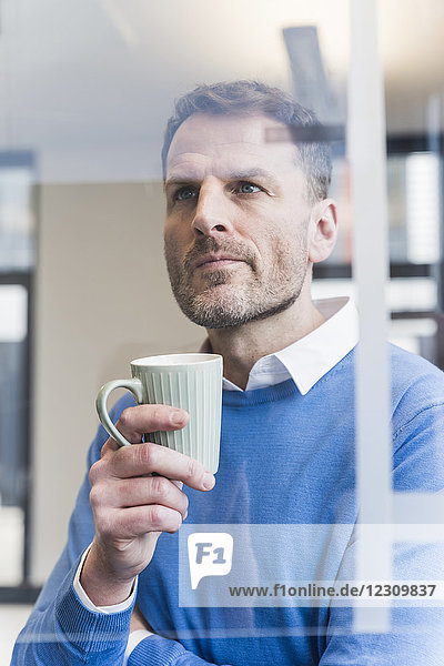 Fokussierter Geschäftsmann hält Tasse Kaffee mit Blick auf die Glasscheibe