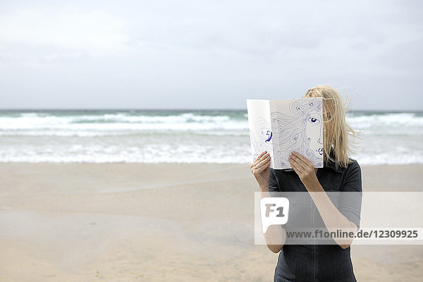 Frau bedeckt Gesicht mit Buch liest Poesie am Strand