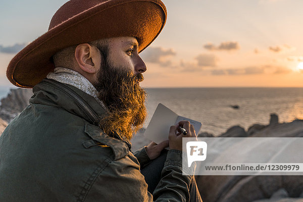 Italy  Sardinia  bearded man with notebook in front of the sea at sunset