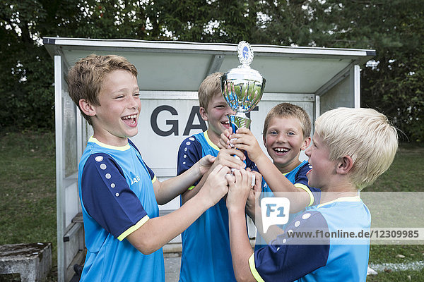 Junge Fußballspieler jubeln mit Pokal