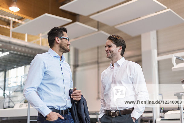 Two smiling businessmen talking in modern factory
