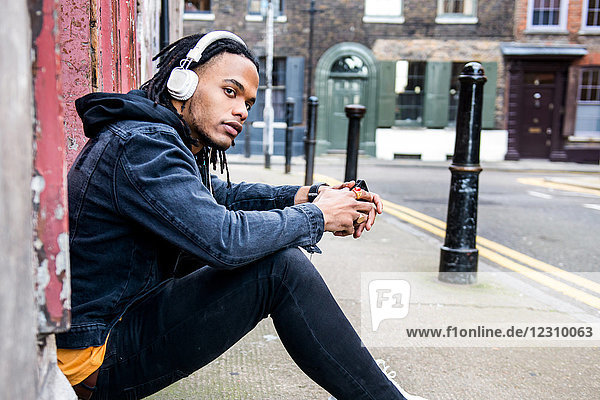 Man sitting in street listening to music through headphones