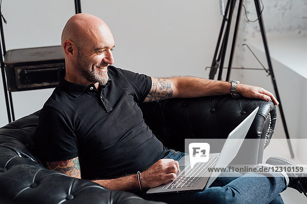 Mann im Sessel mit Laptop lächelt