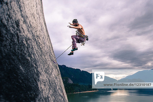 Man with climbing rope jumping off rock face on Malamute  Squamish  Canada