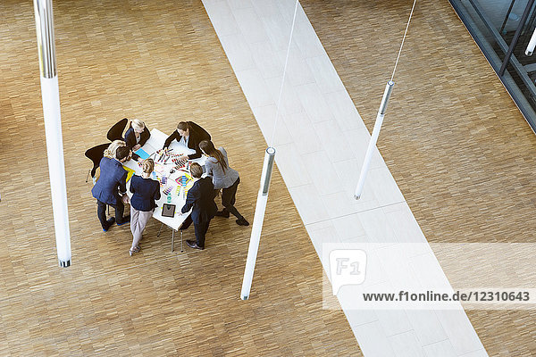 Businesswomen and men in office atrium looking at design swatches on table  high angle view