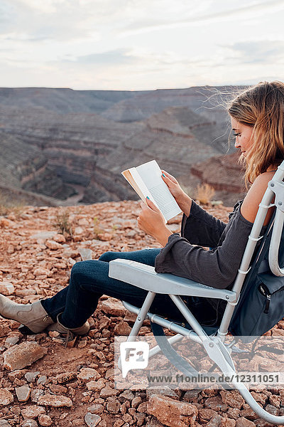 Junge Frau in abgelegener Umgebung  sitzt auf Campingstuhl  liest Buch  Mexican Hat  Utah  USA