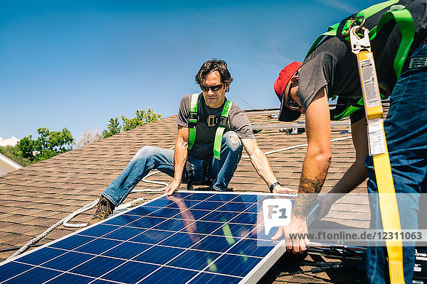 Zwei Handwerker installieren Sonnenkollektoren auf dem Hausdach
