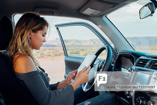 Junge Frau sitzt im Fahrzeug und schaut auf ein digitales Tablet  Mexican Hat  Utah  USA
