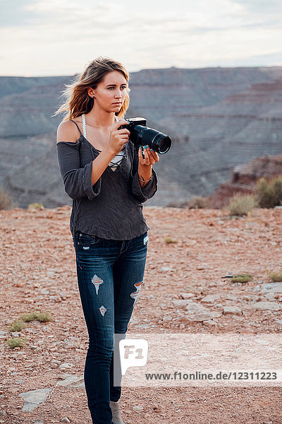 Junge Frau im Freien  hält Spiegelreflexkamera  fotografiert Umgebung  Mexican Hat  Utah  USA