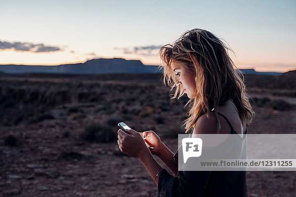Junge Frau in abgelegener Umgebung  die ein Smartphone benutzt  Mexican Hat  Utah  USA