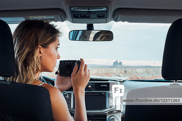 Young woman sitting in vehicle  taking photo through windscreen  using camera  Mexican Hat  Utah  USA