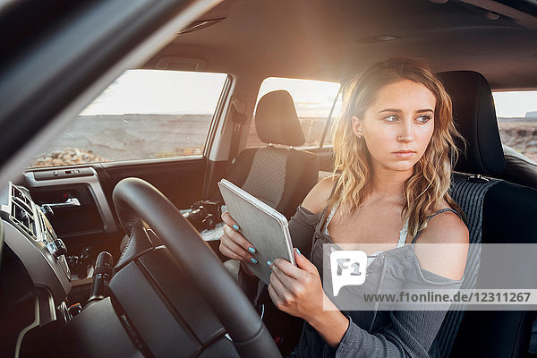 Junge Frau sitzt im Fahrzeug  hält ein digitales Tablet und schaut aus dem Fenster  Mexican Hat  Utah  USA