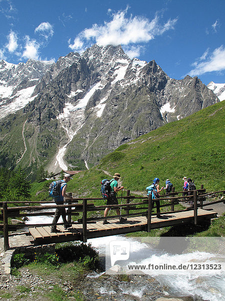 Italia Aoste valley  Ferret valley Courmayeur  a group of hikers is crossing a creek on the tour du mont blanc trail in front of the italian side of the mont blanc range
