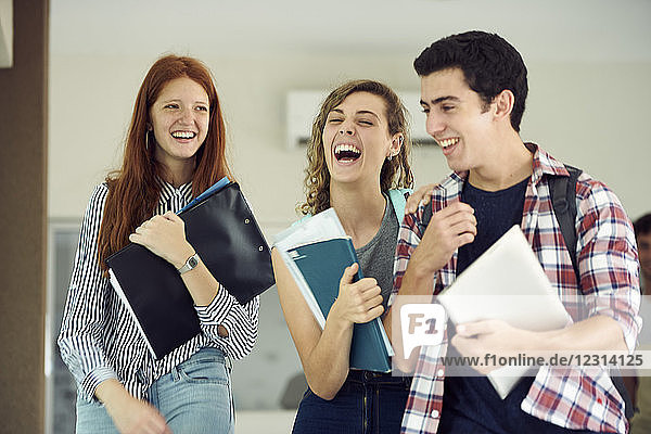Classmates laughing together while walking in school corridor