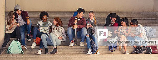 Schüler  die zwischen den Unterrichtsstunden miteinander plaudern und auf ihre Smartphones schauen