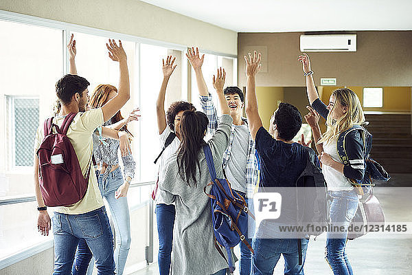 Group of students standing in circle in corridor with hands raised in the air