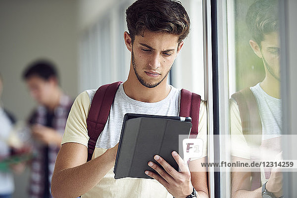 Männlicher Student  der ein digitales Tablet im Korridor benutzt