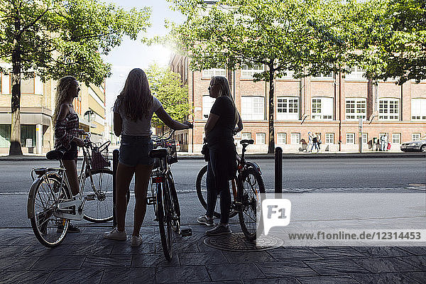 Three teenage girls (14-15) on bicycles talking