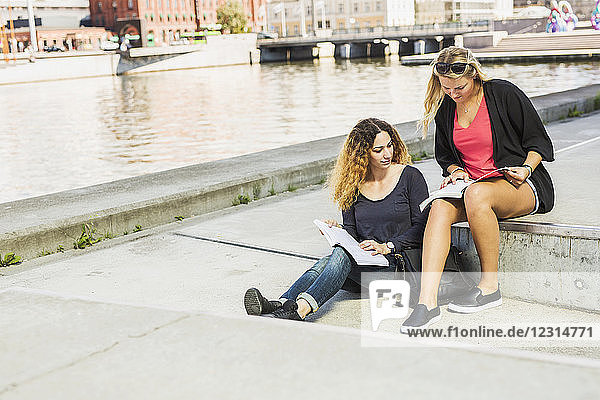 Two young women reading books by river
