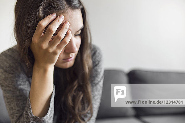 Pensive young woman sitting on sofa