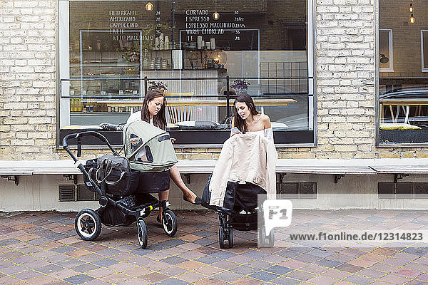 Two young mothers with baby strollers sitting in front of cafe