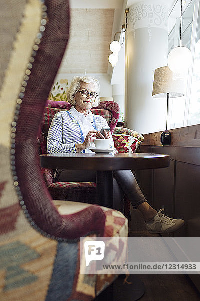 Ältere Frau  die während einer Kaffeepause in einem Café ein Mobiltelefon benutzt