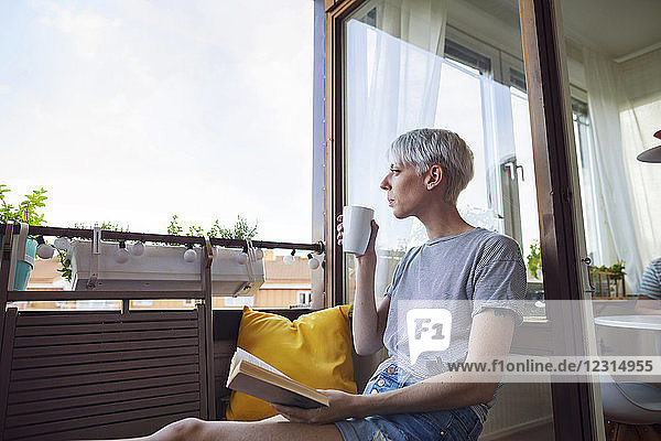 Woman reading book on balcony and drinking coffee