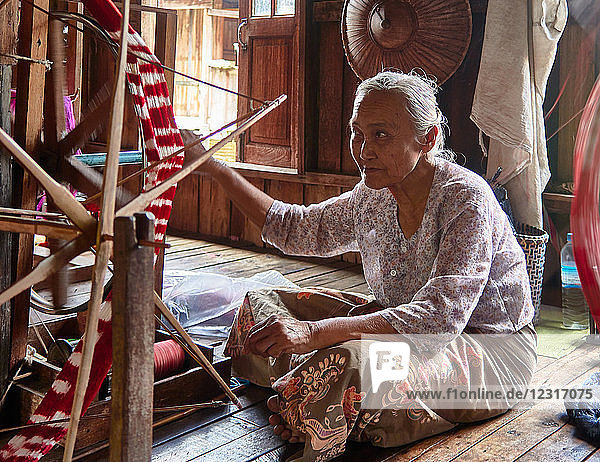 Local women are crafting their products in a textile shop. The material is from the stem of the lotus flowers. The women are working on their weaving chairs.