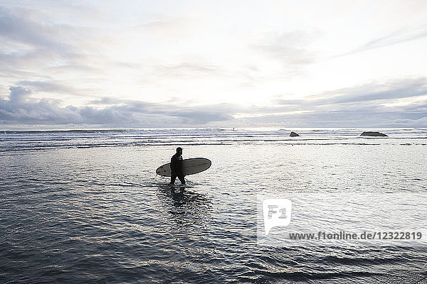 Surfer wading in the water with his surfboard  Southeast Alaska  Yakutat  Alaska  United States of America