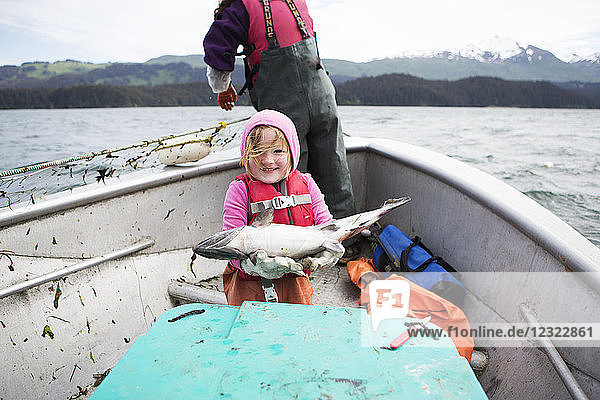 Young girl holding a fresh caught salmon while in her family's set-net skiff with her mother  Seldovia  South-central Alaska; Alaska  United States of America