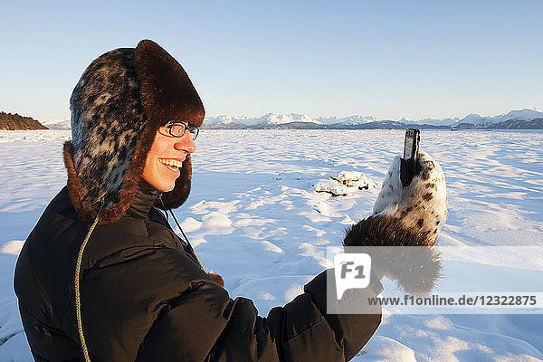 Mann mit Pelzmütze und Fäustlingen steht im Schnee und telefoniert  Süd-Zentral-Alaska; Alaska  Vereinigte Staaten von Amerika