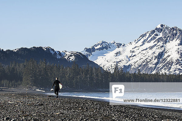 Surfer walking on the beach along the Kenai Peninsula Outer Coast  South-central Alaska  USA