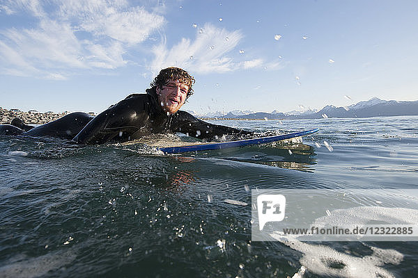 Surfer paddles out into the ocean  Southeast Alaska; Yakutat  Alaska  United States of America