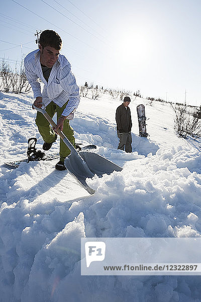Snowboarder clearing snow with a shovel  South-central Alaska  Homer  Alaska  United States of America