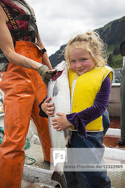 Young girl holding a large red salmon while standing in a set-net skiff  South-central Alaska; Seldovia  Alaska  United States of America