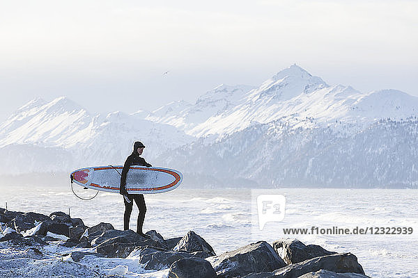 Surfer mit Surfbrett mit Blick auf die Kachemak Bay  Süd-Zentral-Alaska; Homer  Alaska  Vereinigte Staaten von Amerika