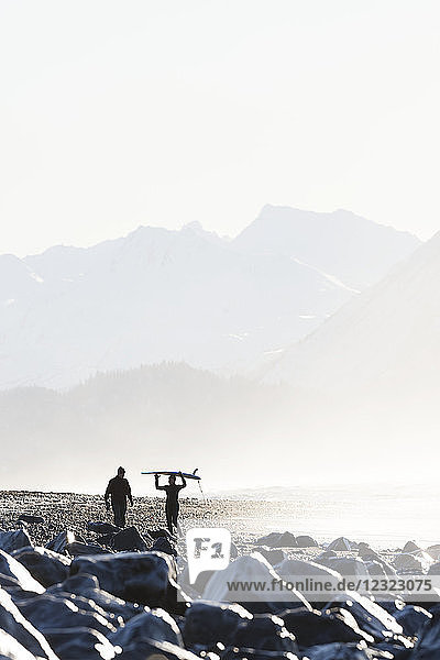 Eine Surferin trägt ihr Surfbrett über dem Kopf am Strand von Homer Spit  Süd-Zentral-Alaska; Homer Spit  Alaska  Vereinigte Staaten von Amerika