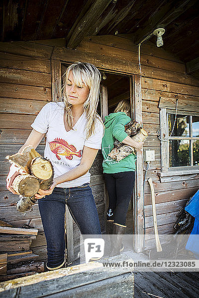 Zwei junge Frauen tragen gehacktes Holz in eine Hütte  Süd-Zentral-Alaska; Homer  Alaska  Vereinigte Staaten von Amerika