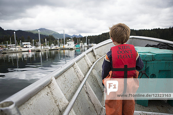 Young boy stands in his family's set-net skiff with a life vest saying 'kids don't float'  South-central Alaska; Seldovia  Alaska  United States of America