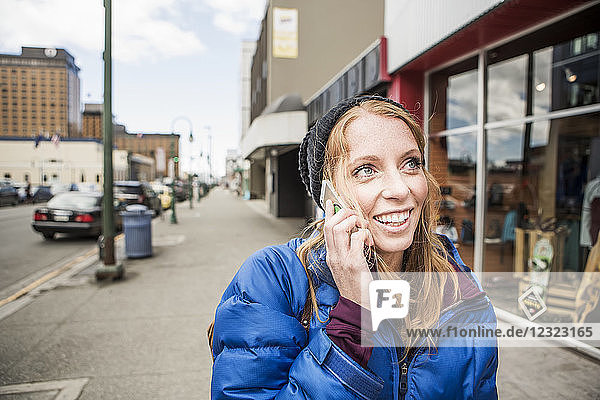 Junge Frau spricht mit ihrem Smartphone in der Innenstadt von Anchorage  Süd-Zentral-Alaska; Anchorage  Alaska  Vereinigte Staaten von Amerika