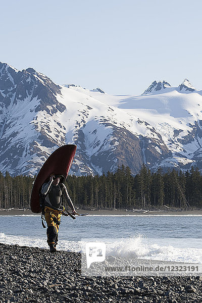 Surfer carrying his surfboard along the Kenai Peninsula Outer Coast  South-central Alaska; Alaska  United States of America