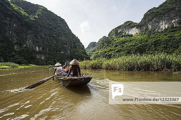 People in a boat on the Ngo Dong River surrounded by limestone karst mountains; Tam Coc  Ninh Binh  Vietnam