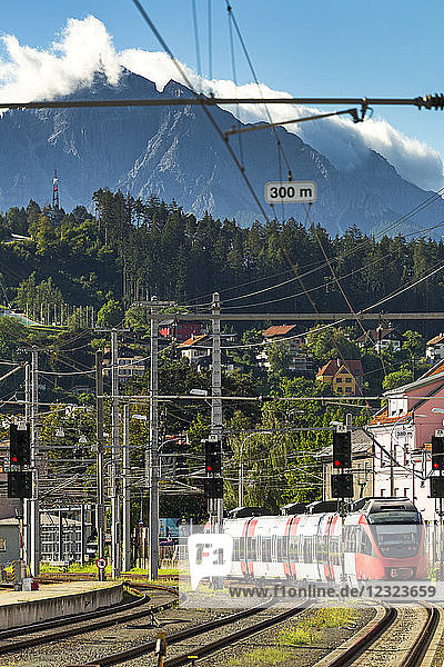 Elektrischer Dieselzug  der sich dem Bahnsteig nähert  mit Bergen im Hintergrund und blauem Himmel; Innsbruck  Österreich