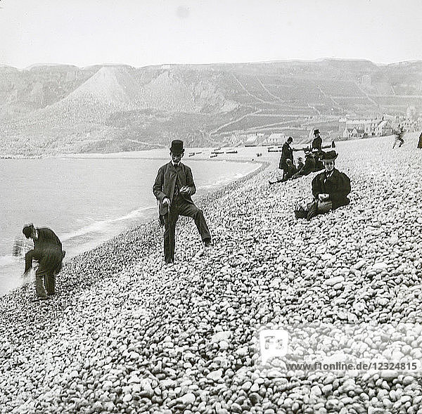 Magic lantern slide circa 1900.Victorian/Edwardian.Social History.Chesil Beach   sometimes called Chesil Bank  in Dorset  southern England is one of three major shingle structures in Britain.[1] Its toponym is derived from the Old English ceosel or cisel  meaning 'gravel' or 'shingle' The beach is often identified as a tombolo  although research into the geomorphology of the area has revealed that it is in fact a barrier beach which has 'rolled' landwards  joining the mainland with the Isle of Portland  giving the appearance of a tombolo.[2] The shingle beach is 29 kilometres (18 mi) long  200 metres (660 ft) wide and 15 metres (50 ft) high. The beach and The Fleet  a shallow tidal lagoon [3] are part of the Jurassic Coast  a UNESCO World Heritage Site  and the location for a 2007 novel  On Chesil Beach by Ian McEwan.