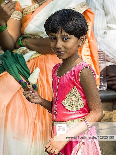 Ein junges Mädchen in einem leuchtend rosa Kleid isst ein Eis am Stiel und lächelt in die Kamera; Mumbai  Maharashtra  Indien